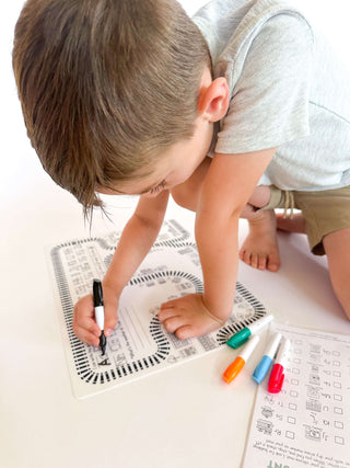 A young boy coloring on a train-themed activity sheet with colorful markers.