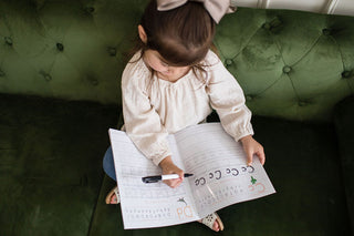 Child practicing writing letters in a dry erase alphabet book on a green couch, promoting interactive learning.
