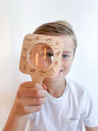 6 year old using a magnifying glass to explore bugs during outdoor science play