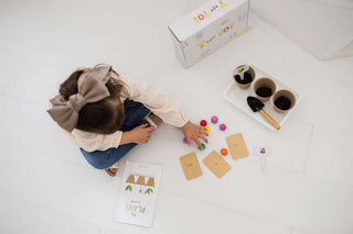 Young girl with a bow sitting on the floor using the gardening kit with pots, seeds and colorful balls.