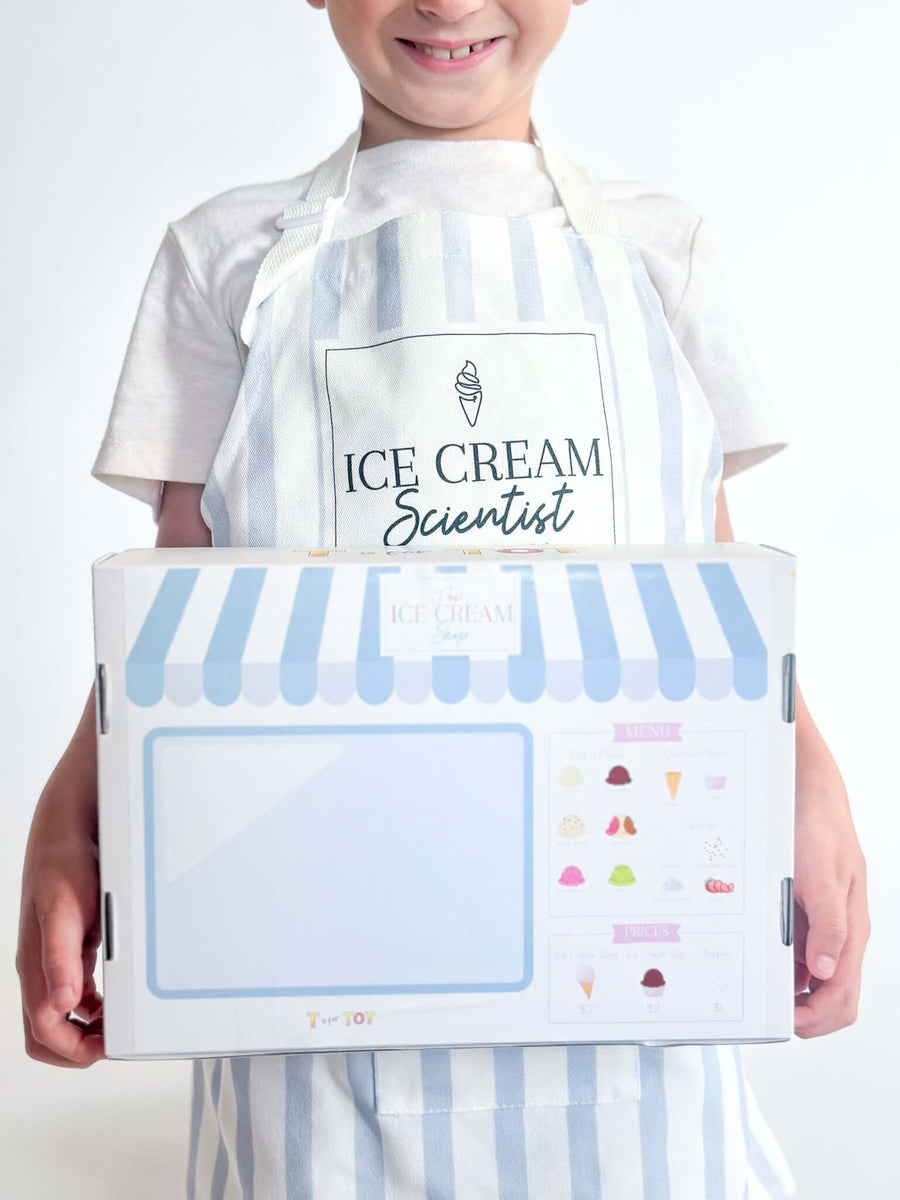 Child wearing an 'Ice Cream Scientist' apron holding an ice cream kit with colorful graphics. in action